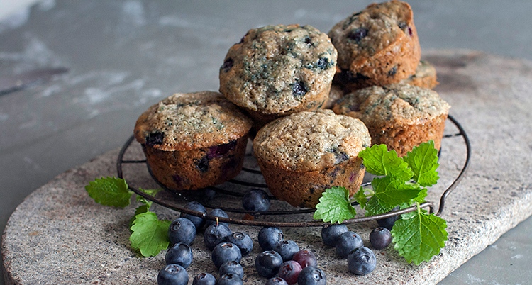 Bilden visar ett fat. På fatet ligger flera muffins. Bredvid ligger det blåbär.