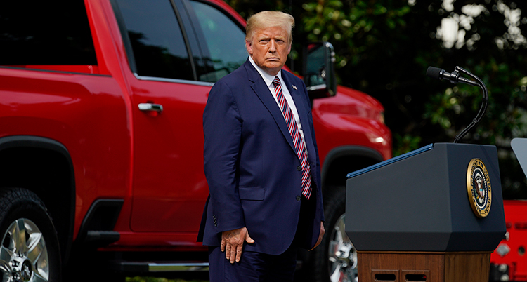 Donald Trump har blå kostym och står framför en röd bil.