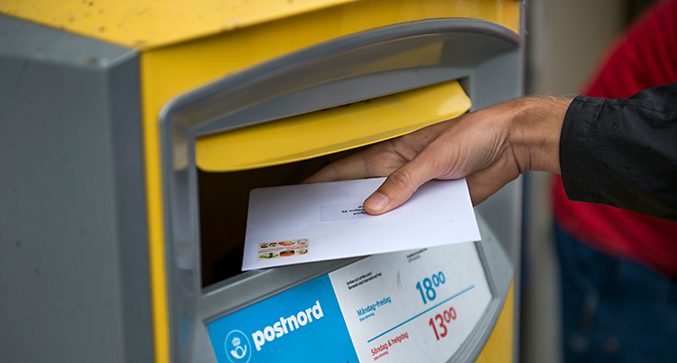 En person lägger ett brev i en gul postlåda.