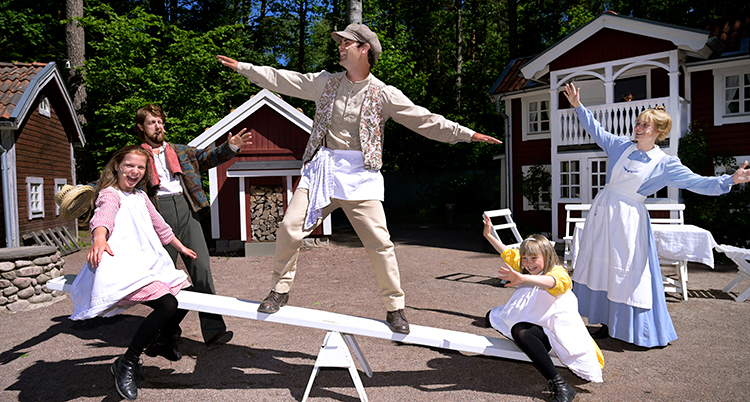 Barnskådespelare framför några röda stugor gungar på en gungbräda.