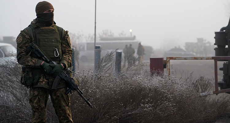 En man i militärkläder och svart mask för ansiktet står och håller i ett vapen.