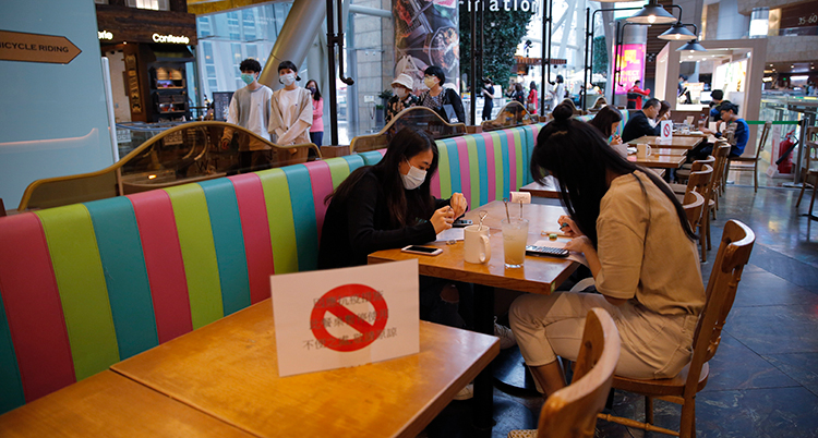 Två personer med munskydd sitter vid ett cafébord i Hongkong. Bordet bredvid har en skylt med förbud att sätta sig.