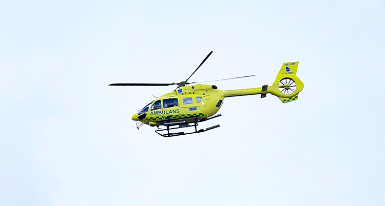 Vi ser en gul helikopter i luften. Det står Ambulans på helikoptern.