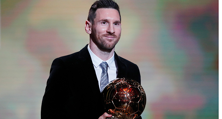 Fotbollsspelaren Lionel Messi håller i priset Guldbollen. Det ser ut som en rödsprakande fotboll.