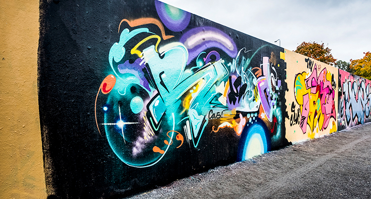 En vägg med graffiti i bland annat turkost och lila på en svart vägg.