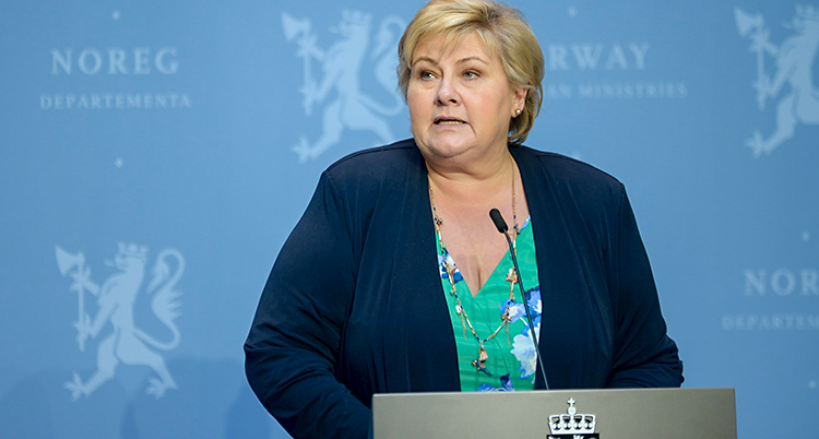 Hon står och pratar till journalister. Hon står vid ett bord där det finns en mikrofon.