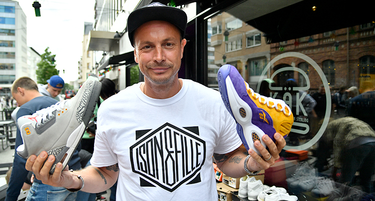 Petter håller upp två skor, två sneakers. En är lila och en vit.