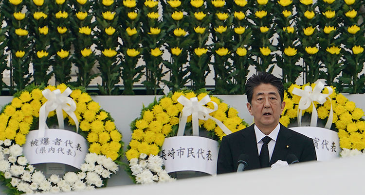 Japans premiärminister Shinzo Abe håller tal. Bakom honom hänger kransar med gula och vita blommor.