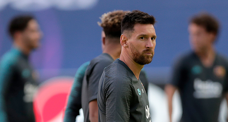 Lionel Messi är på en fotbollsplan. Det är träning. Han har en grå tröja på sig. På sin högra arm har han tatueringar.