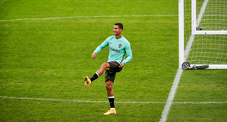 Cristiano Ronaldo är på en fotbollsplan. Han har precis sparkat iväg en boll. Han ler och är glad.