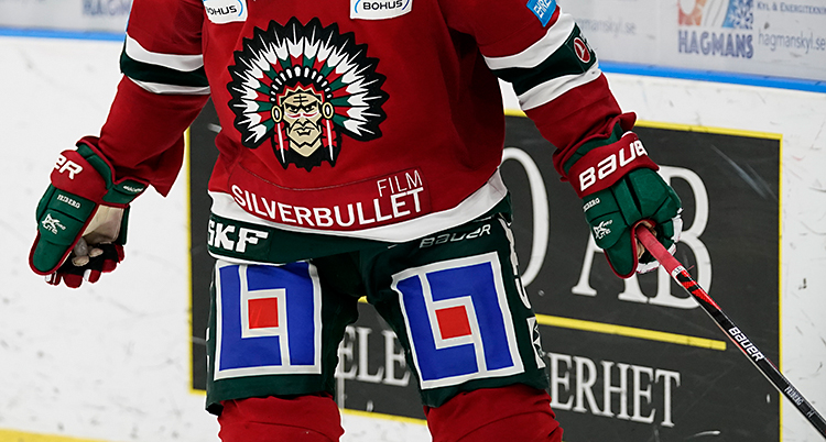 En ishockeyspelare på isen. Han har en röd tröja. På tröjan finns en person från urbefolkningen i Amerika, med fjädrar på huvudet.