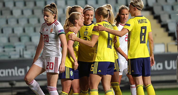 Flera spelare står i en grupp och kramar om varandra. En av dem har gjort mål i fotboll. De har gula t-shirts och blå shorts.