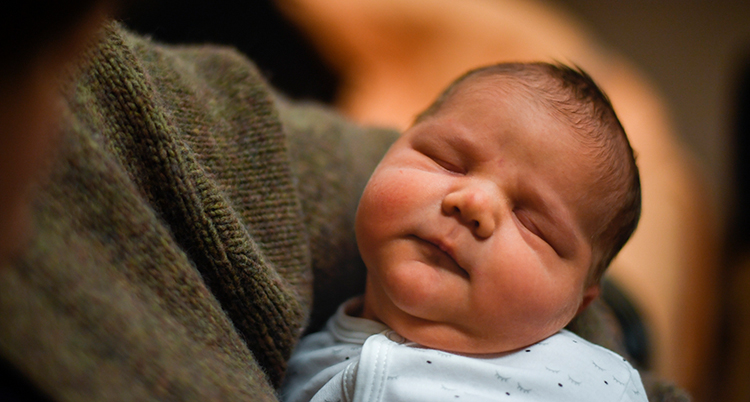 En liten bebis vilar en en vuxen famn.