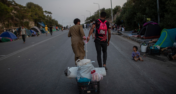 Två personer drar en liten korg med packning på en gata i Lesbos.