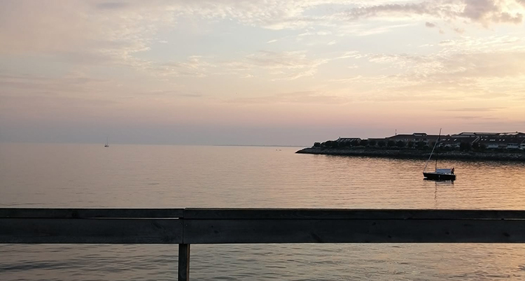 Det är skymning. Himlen är ljust rosa. En båt syns ute på vattnet.