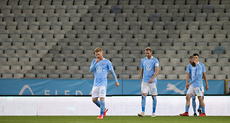 Bilden visar en stadion för fotboll. Några spelare går på gräset. De hänger med sina huvuden och ser ledsna ut. De har ljusblå tröjor och vita shorts.