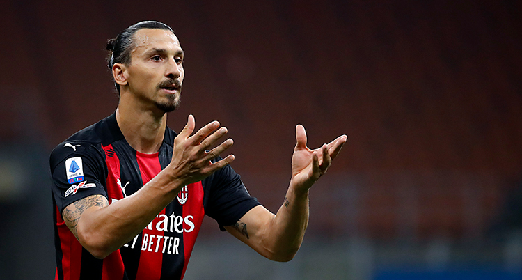 Zlatan har en randig tröja i rött och svart. Han har håret i en knut bak på huvudet.