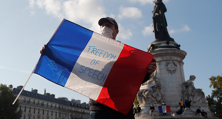 En man som protesterar i Paris håller upp en flagga där det står freedom of speech.
