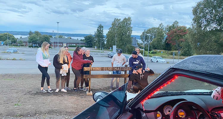 De står vid ett staket på en parkeringsplats. En del av en epatraktor syns på bilden.