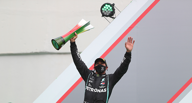 Lewis Hamilton sträcker armarna mot luften. I ena handen har han en pokal.