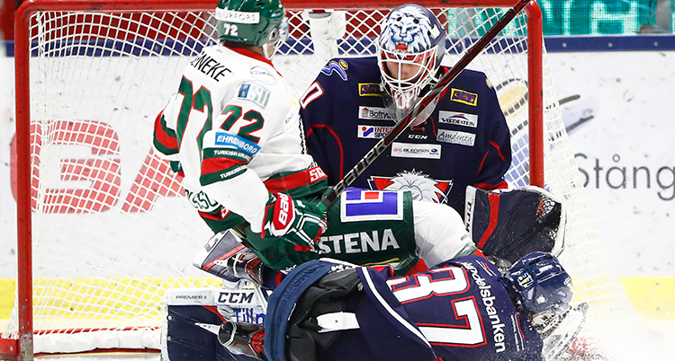Hockeyspelare i hockeyutrustning ligger på varandra framför målvakten i ett hockeymål
