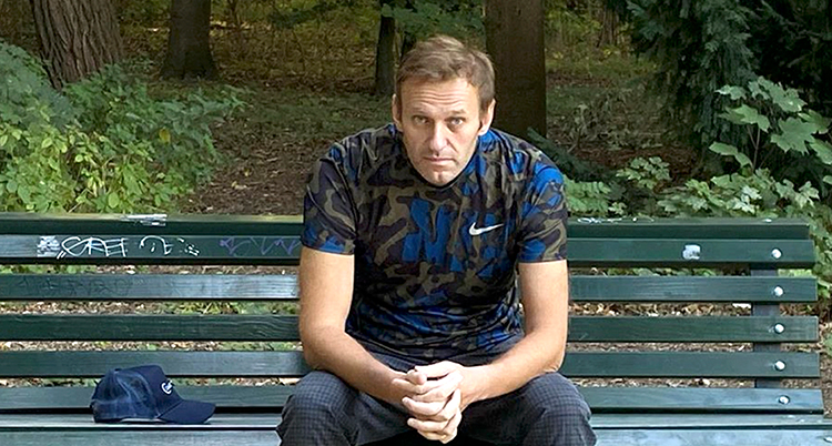 Han sitter på en parksoffa men händerna knäppta i knät. Han tittar in i kameran och ser allvarlig ut.