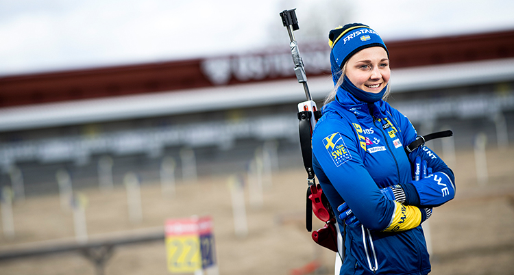 Stina Nilsson står med armarna i kors. På ryggen har hon ett gevär för skidskytte.