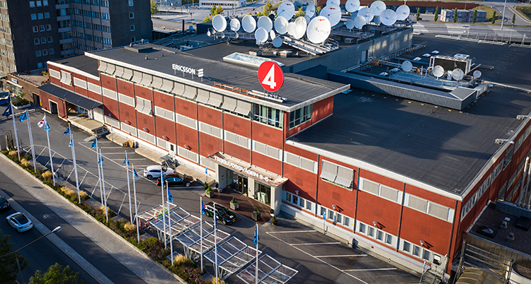 Vi ser TV4s hus i Stockholm. Det är ett stort rött hus. Ovanpå huset finns många parabolantenner. Bilden är tagen uppifrån.