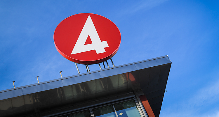 Vi ser toppen på ett hus. På taket sitter en stor rund skylt. Den är röd och det är en vit fyra på skylten.