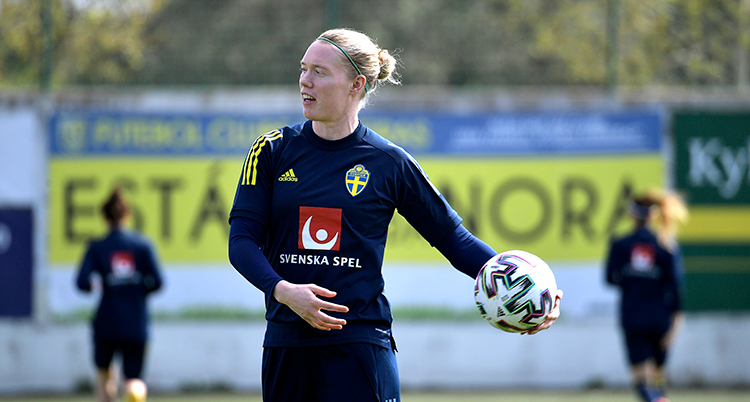 Hon har en blå tröja och fotbollsmålvaktshandskap, hon ska slänga iväg en fotboll.