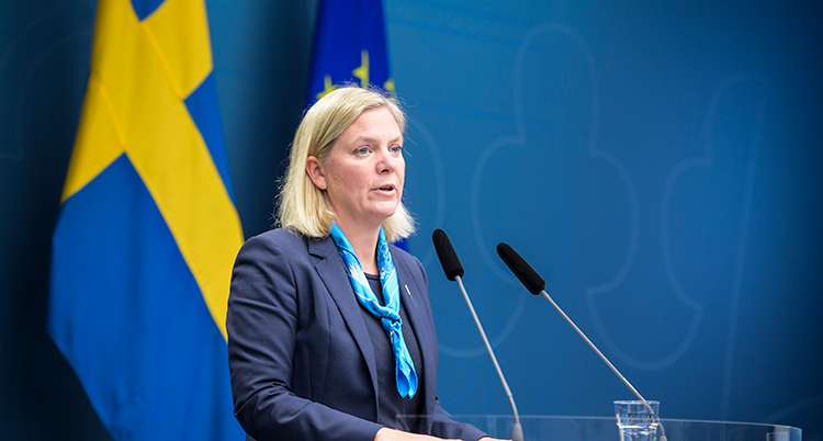 Hon har marinblå kavaj. Hon talar framför två mikrofoner.