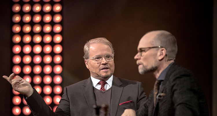 De sitter i en tv-studio. De har kostym på sig. Bakom dem syns många lampor.