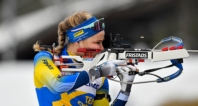 Stina siktar med et gevär som hon håller mot kinden.