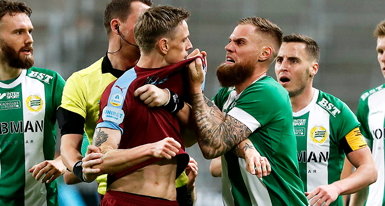 en fotbollsspelare i grön tröja ser arg ut och tar ett hårt tag om en annan fotbollsspelares tröja