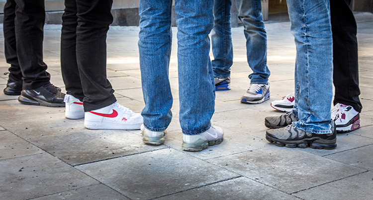 Sex unga jeansklädda benpar syns i en grupp, alla bär sneakers.
