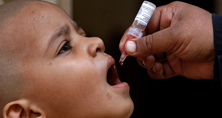 Ett barn gapar och över munnen håller en vuxen hand en vaccinationsspruta