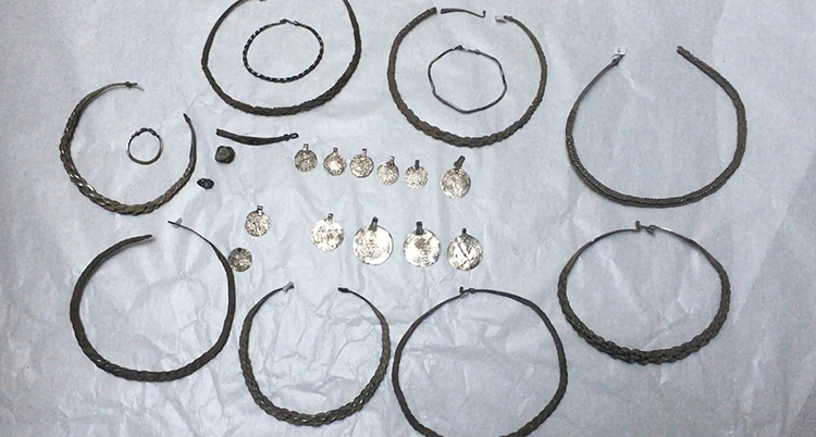 Ett antal silverhalsband och ringar ligger på en vit duk