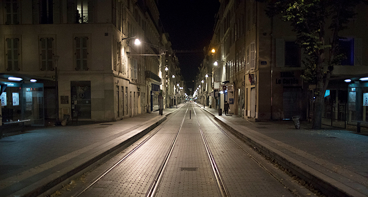 Det är kväll. Vi ser en gata i staden Marseille. Gatan är helt tom. Mitt i gatan finns spår för spårvagnar. Bredvid gatan finns hus. Några gatlampor lyser upp i mörkret.