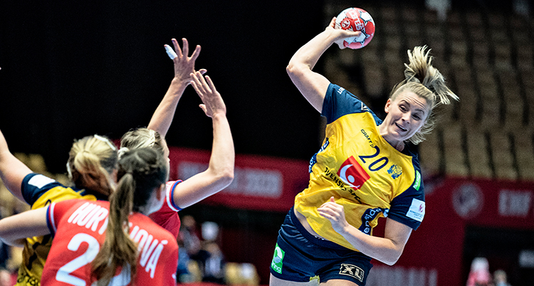 En kvinna med gul landslagströja hoppar upp i luften för att skjuta, hon har höger hand bakom huvudet och är beredd att skjuta handbollen