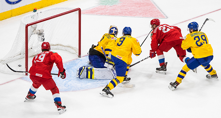 Ishockeyspelare i röda och gula tröjor framför målet. En spelare i rött har gjort mål.
