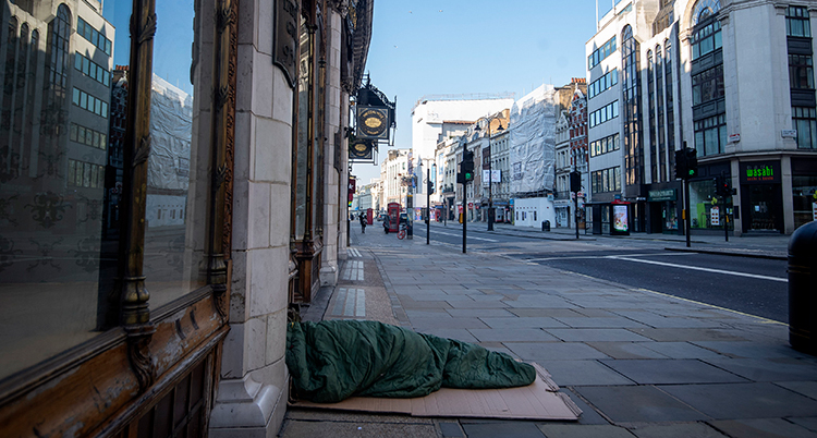 En person sover under ett täcke mitt på gatan i London.