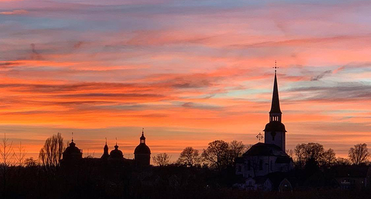 Siluetterna av ett slott och en kyrka och träds syns i svart mot en rosaröd himmel.