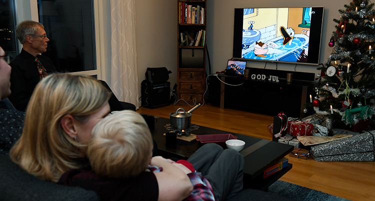 Huvudet på en kvinna och ett litet barn syns i en soffa. De tittar på en tv med Kalle Anka som badar i rutan.