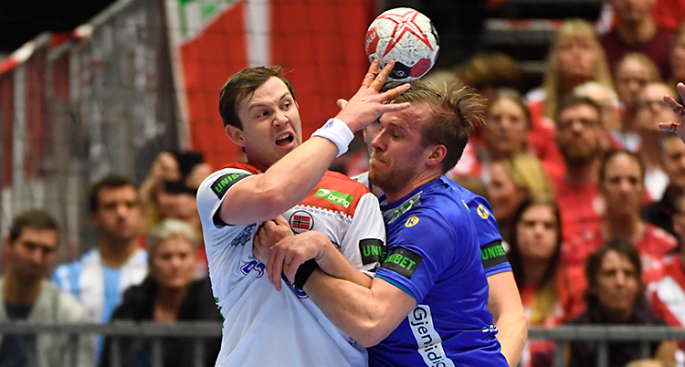 Bilden är från en match i handboll. Två spelare kämpar om bollen. En spelare har en vit tröja. Den andra har en blå tröja.