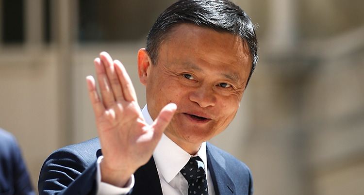 En bild på Jack Ma. Bilden är tagen utomhus. Han ler och vinkar mot kameran. Han har kort svart hår och kostym.