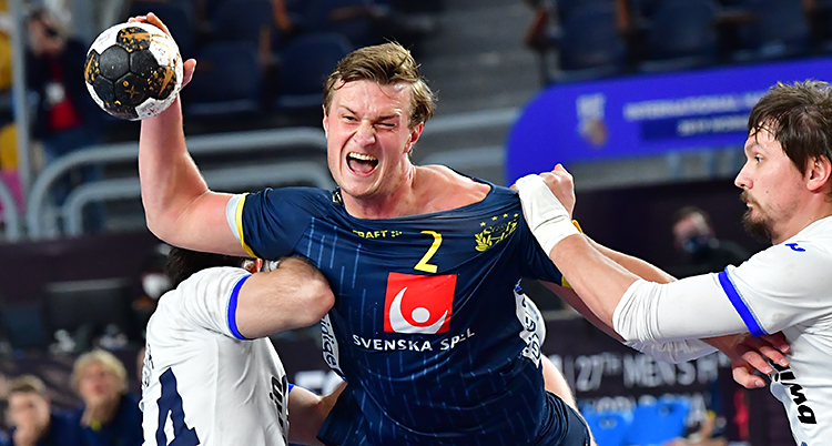 Det är en match i handboll. Den svenska spelaren Jonathan Carlsbogård håller i bollen. Han har en blå tröja. En rysk spelare sliter honom i tröjan.