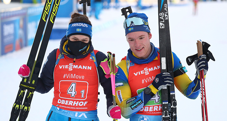 De stor bredvid varandra med skidor ai händerna. Sebastian ler. Hann har ett svart munskydd.