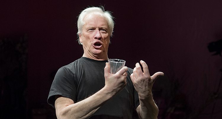 Han håller ett glas vatten i höger hand och formar läpparna i sång.