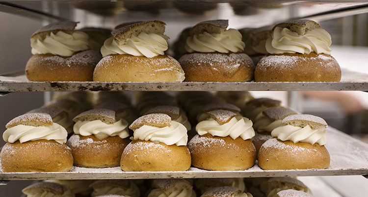 Flera plåtar med semlor står på en vagn i ett bageri