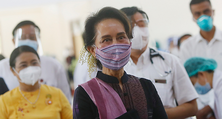 Aung San Suu Kyi gör ett besök hos personal som jobbar med sjukvård och viruset corona. Flera i personalen står runt henne med munskydd. Aung San Suu Kyi har också ett munskydd som är lila.